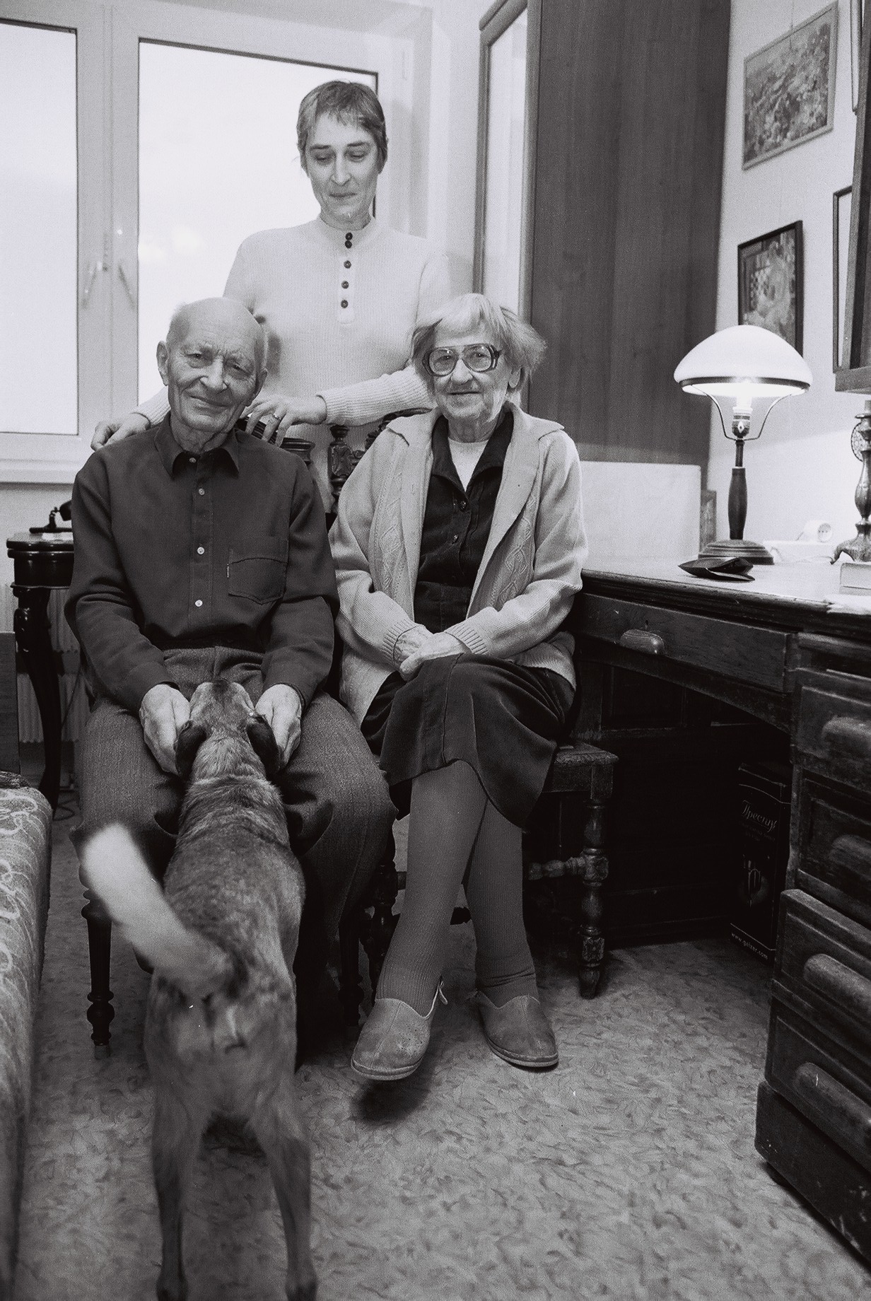 Auf dem Bild sind drei Menschen zu seine, ein älteres Paar und eine Frau. Das Paar sitzt, die Frau steht hinter ihnen. Sie ist ihre Tochter. Der Mann streichelt die Schnauze eines Hundes. Das Bild ist schwarzweiß, es wurde in Moskau im Winter 2004 aufgenommen.